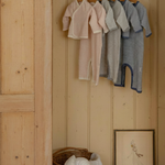 Wooden wardrobe with striped baby onesies clothes in pink, gray, navy blue hanging on a rack inside.