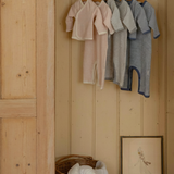 Wooden wardrobe with striped baby onesies clothes in pink, gray, navy blue hanging on a rack inside.