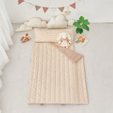 Tan Beige quilted portable nap mat blanket with a white rabbit plush toy on a light gray surface, with decorative elements like clouds and a banner in the background.