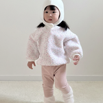 Child wearing a white hooded outfit with pink pants on a plain background