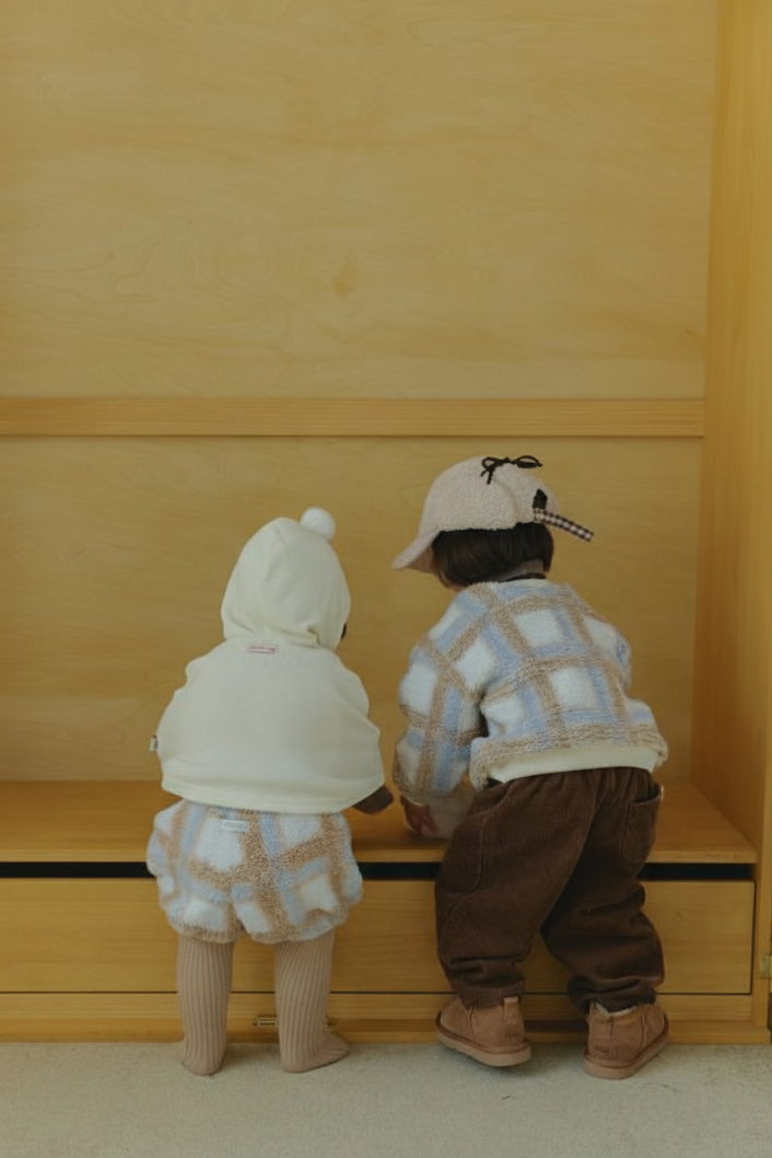 Two children standing in front of a wooden cabinet, wearing winter clothing.