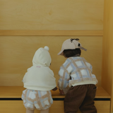 Two children standing in front of a wooden cabinet, wearing winter clothing.