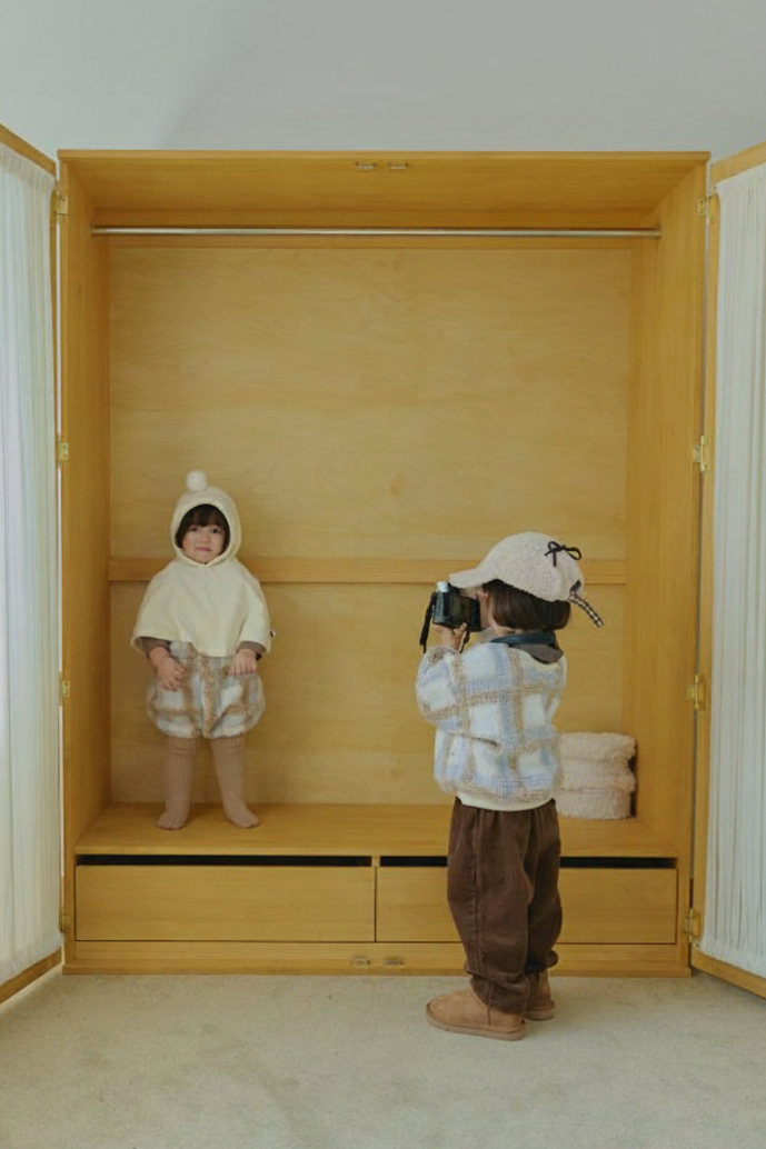 Two children in a room with wooden shelves and white curtains.