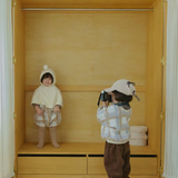 Two children in a room with wooden shelves and white curtains.