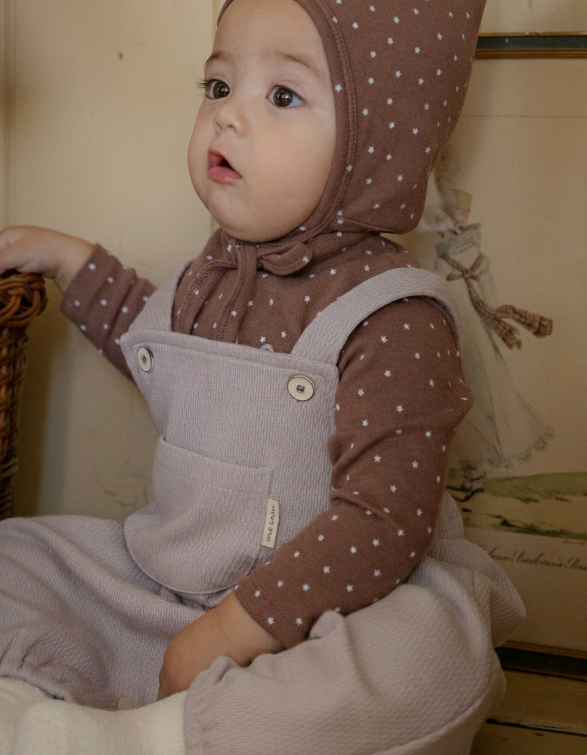 Baby wearing a brown polka dot outfit with a matching bonnet indoors and knitted romper.