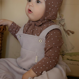 Baby wearing a brown polka dot outfit with a matching bonnet indoors and knitted romper.