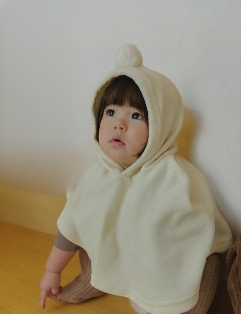 Child wearing a velour beige hooded cape outfit sitting on a wooden floor.