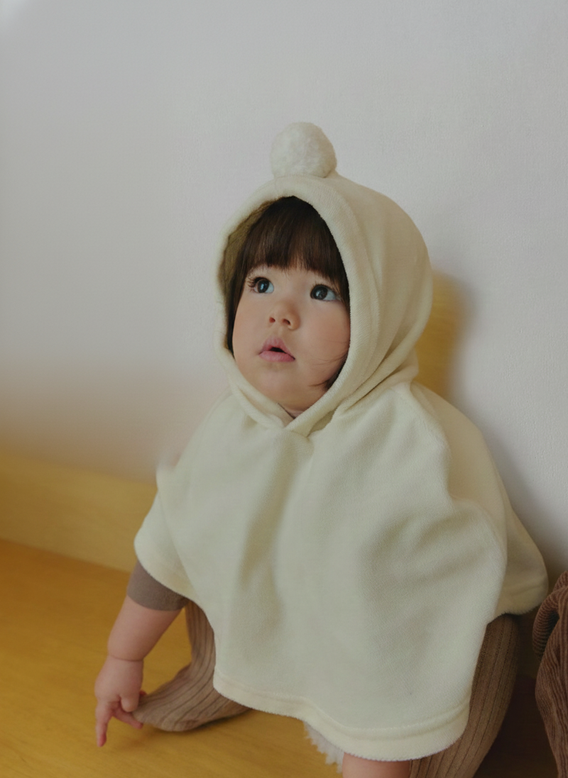 Child wearing a velour beige hooded cape outfit sitting on a wooden floor.