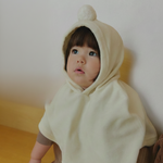 Child wearing a velour beige hooded cape outfit sitting on a wooden floor.