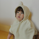 Child wearing a velour beige hooded cape outfit sitting on a wooden floor.