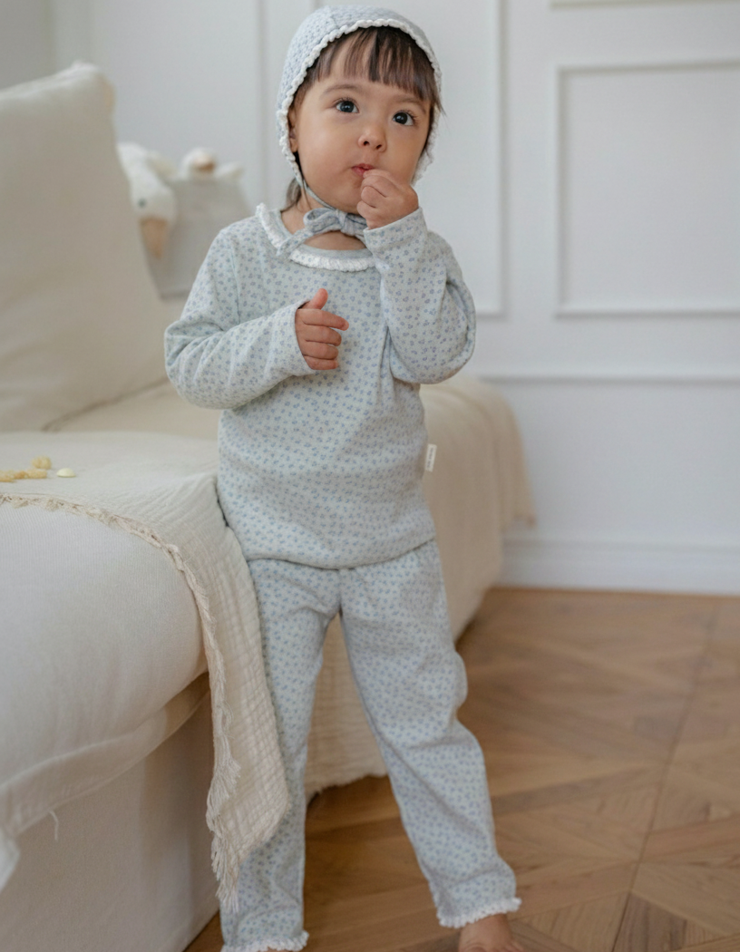 A girl wearing a floral printed mint blue pajama standing in a room with a white couch and wooden floor.