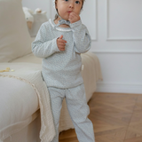 A girl wearing a floral printed mint blue pajama standing in a room with a white couch and wooden floor.