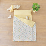 Baby portable nap mat blanket with yellow striped and blue pink bunny rabbit pattern on a wooden floor with toys and a plant.
