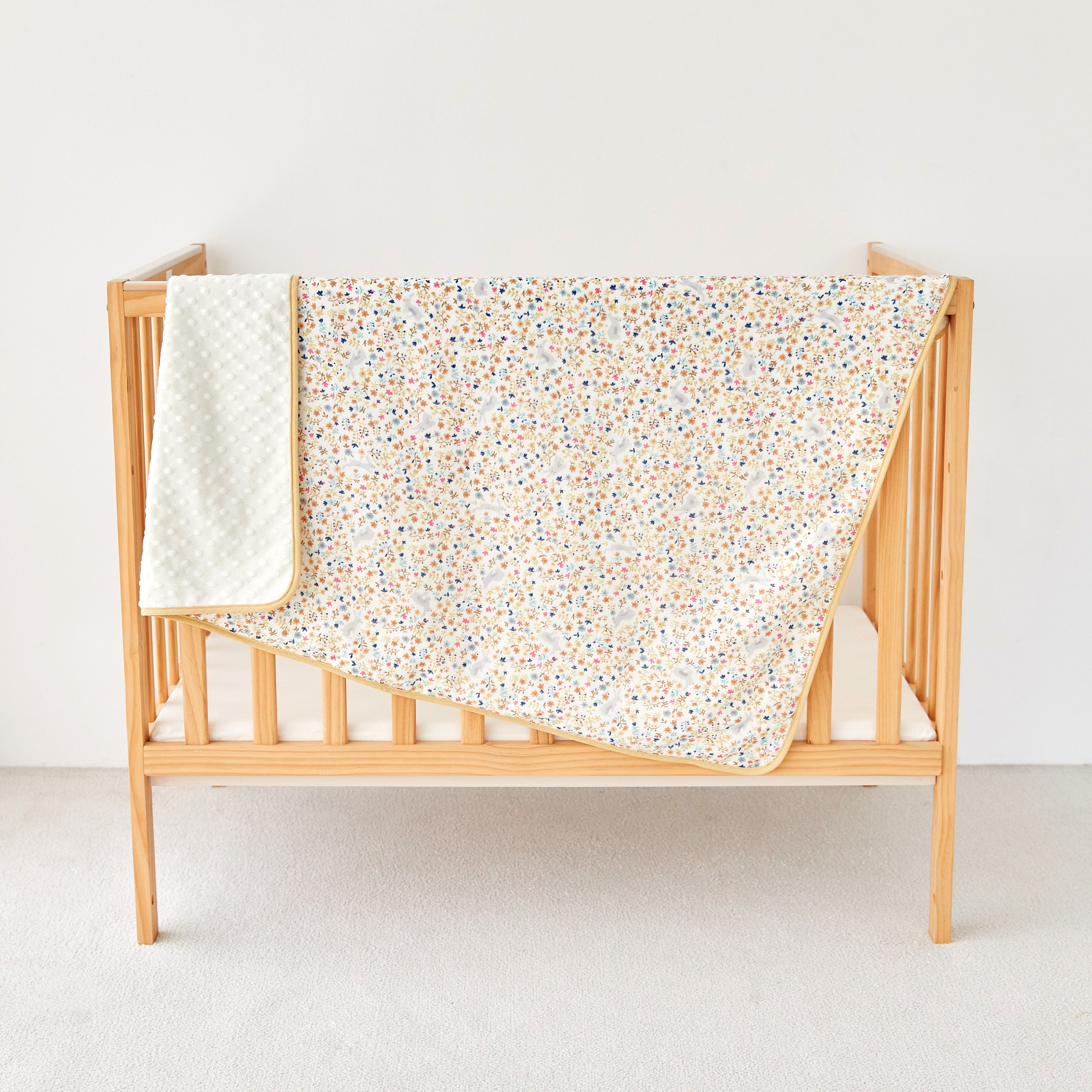 Wooden crib with a rabbit floral-patterned blanket on a white background