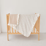 Wooden crib with a beige and ivory ruffled blanket on a light background