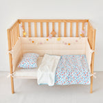 Wooden crib with blue red floral baby bedding including a quilt, pillow, and bumper pad on a light background.