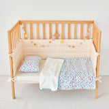 Wooden crib with blue red floral baby bedding including a quilt, pillow, and bumper pad on a light background.