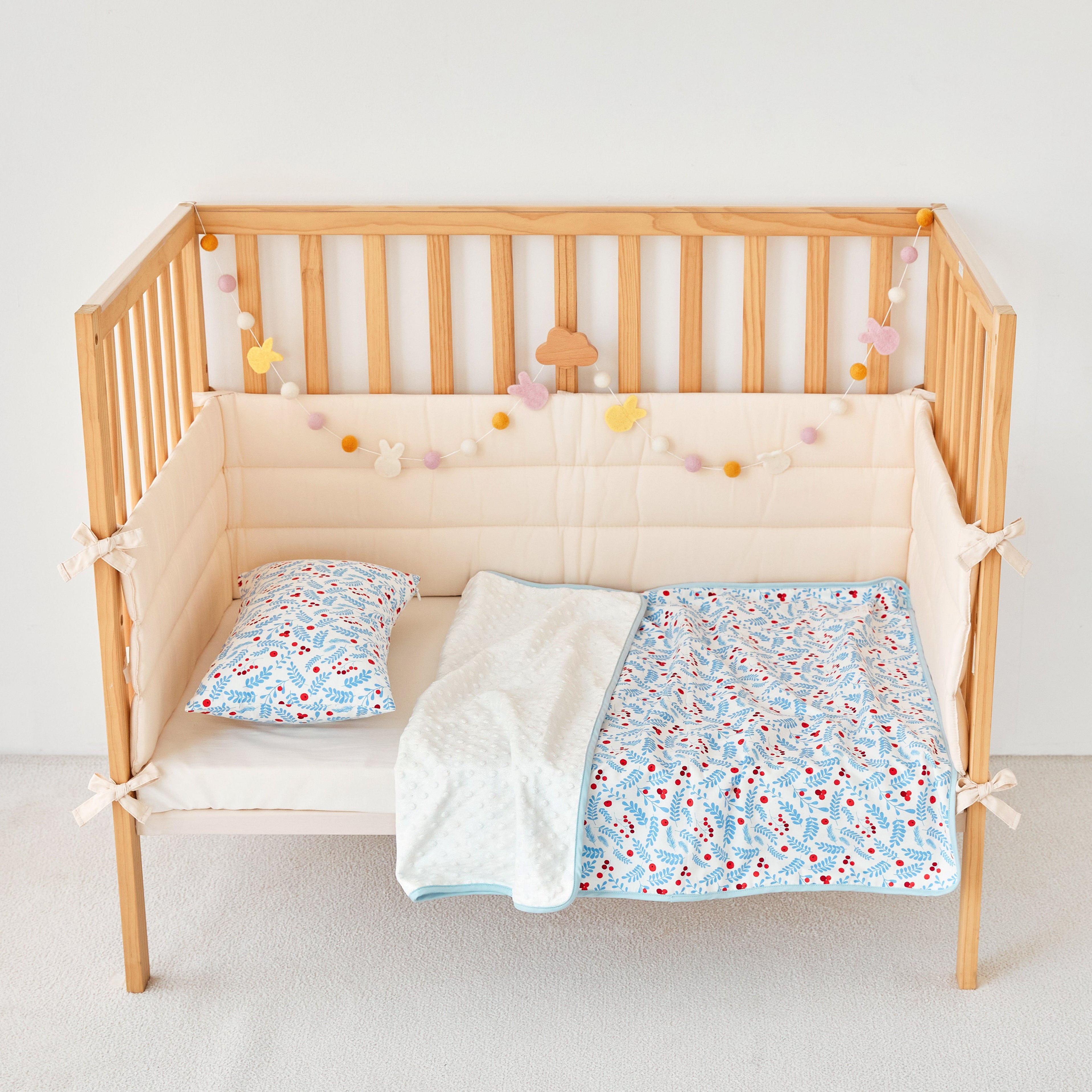 Wooden crib with blue red floral baby bedding including a quilt, pillow, and bumper pad on a light background.