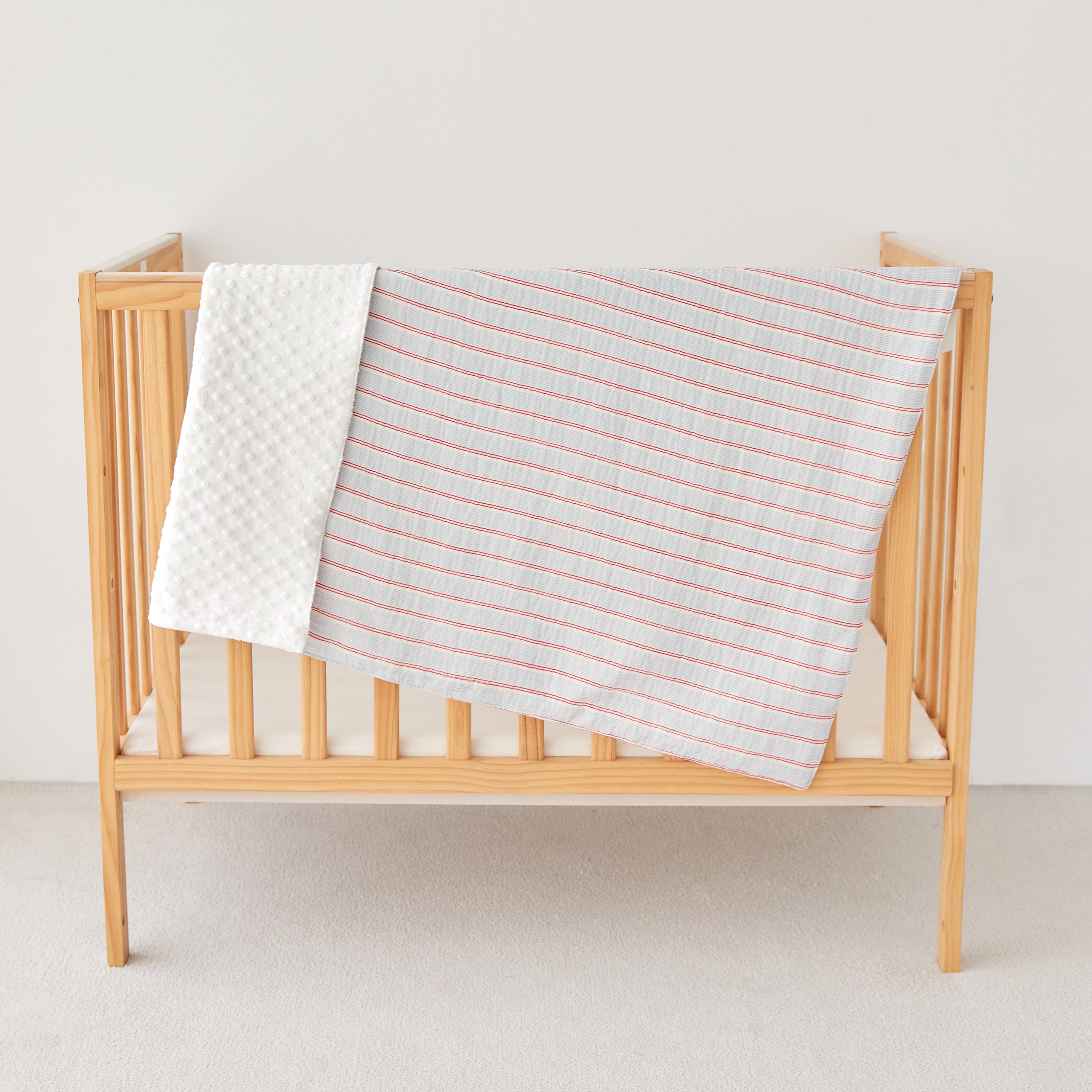 Wooden crib with light blue red striped baby blanket on a plain background