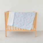 Wooden crib with a blue coral floral blanket and white coverlet on a plain background