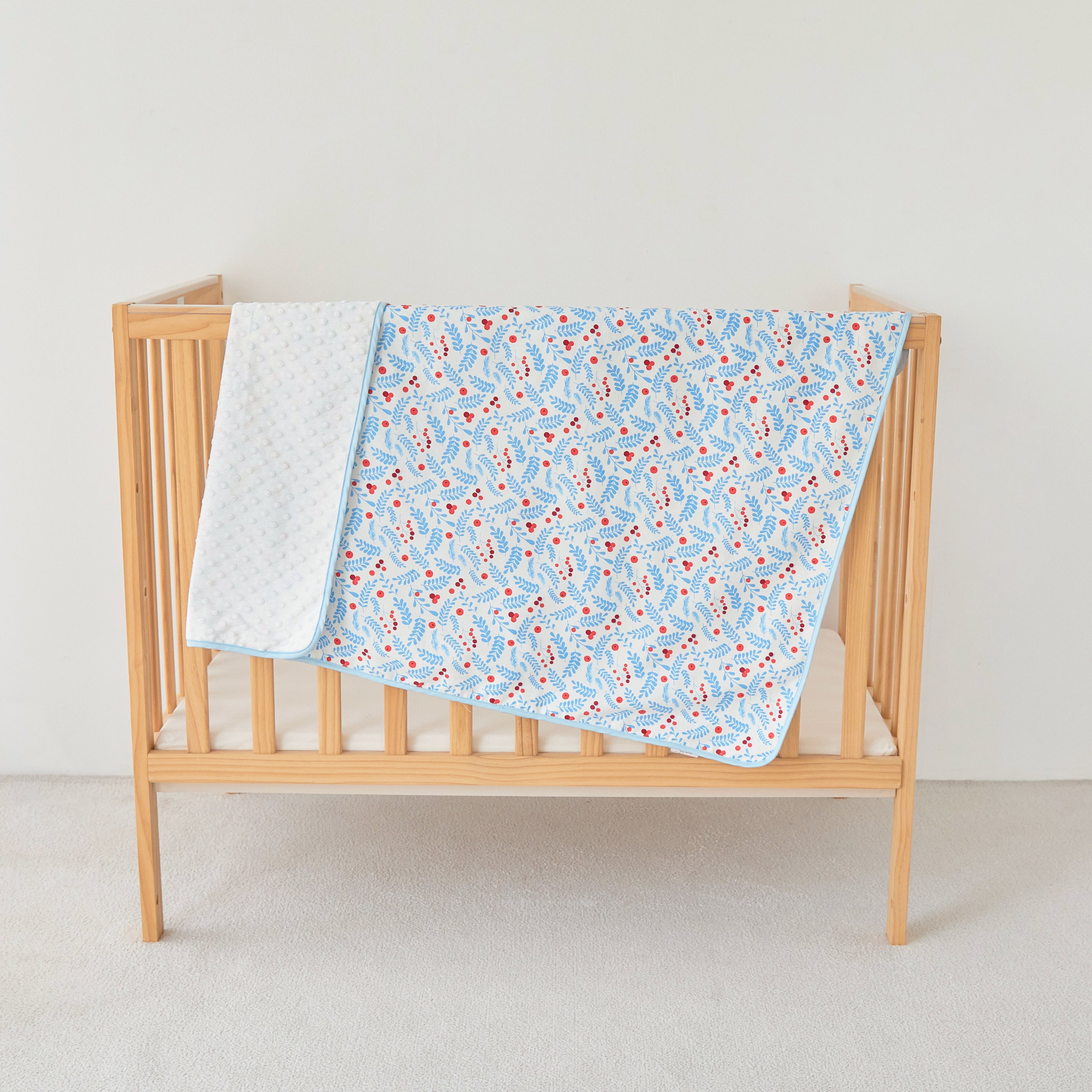 Wooden crib with a blue coral floral blanket and white coverlet on a plain background