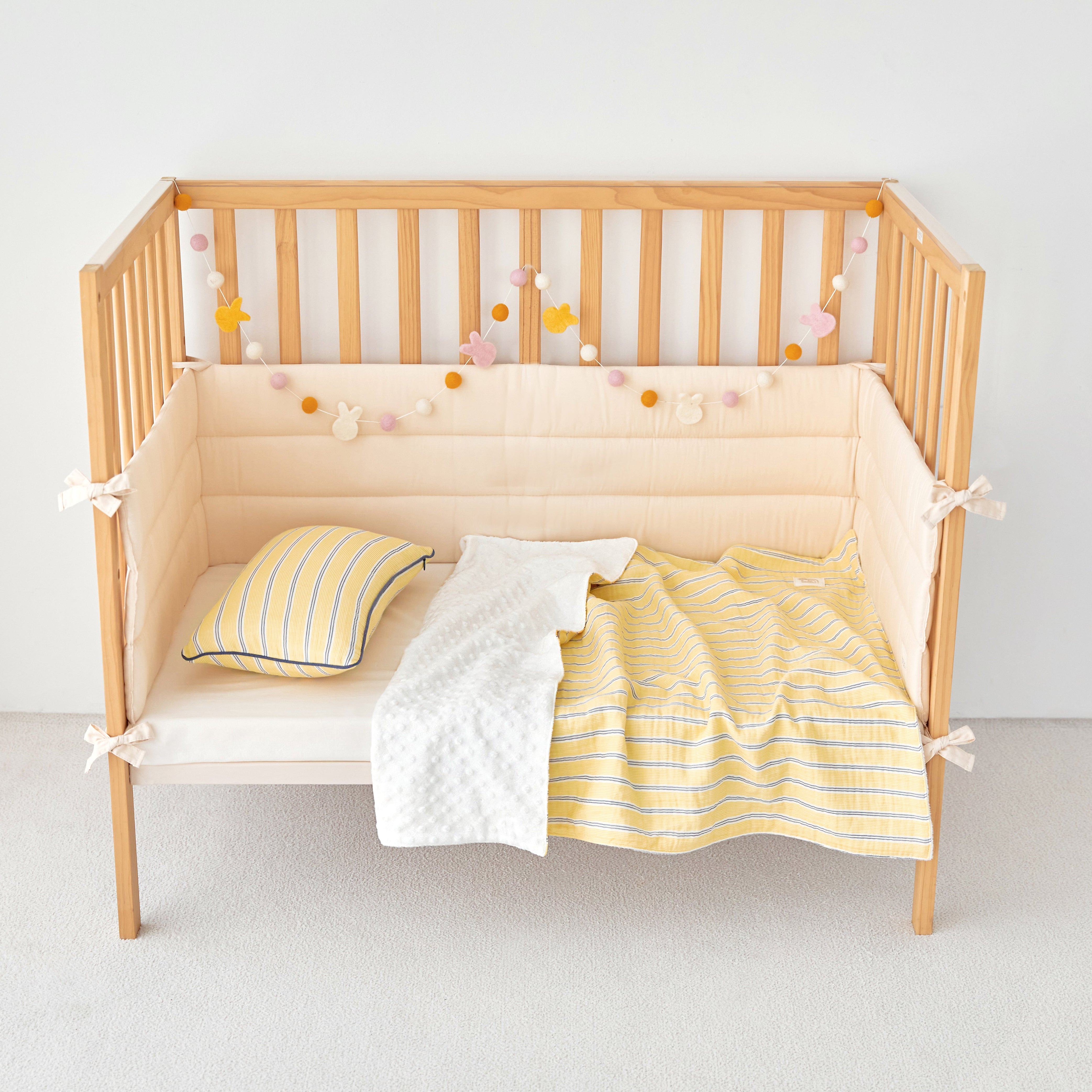 Wooden crib with yellow and white striped gauze minky blanket and decorative pillows on a plain background
