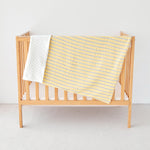 Wooden crib with a yellow baby striped  gauze minky blanket on a light background