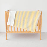 Wooden crib with a yellow baby striped  gauze minky blanket on a light background