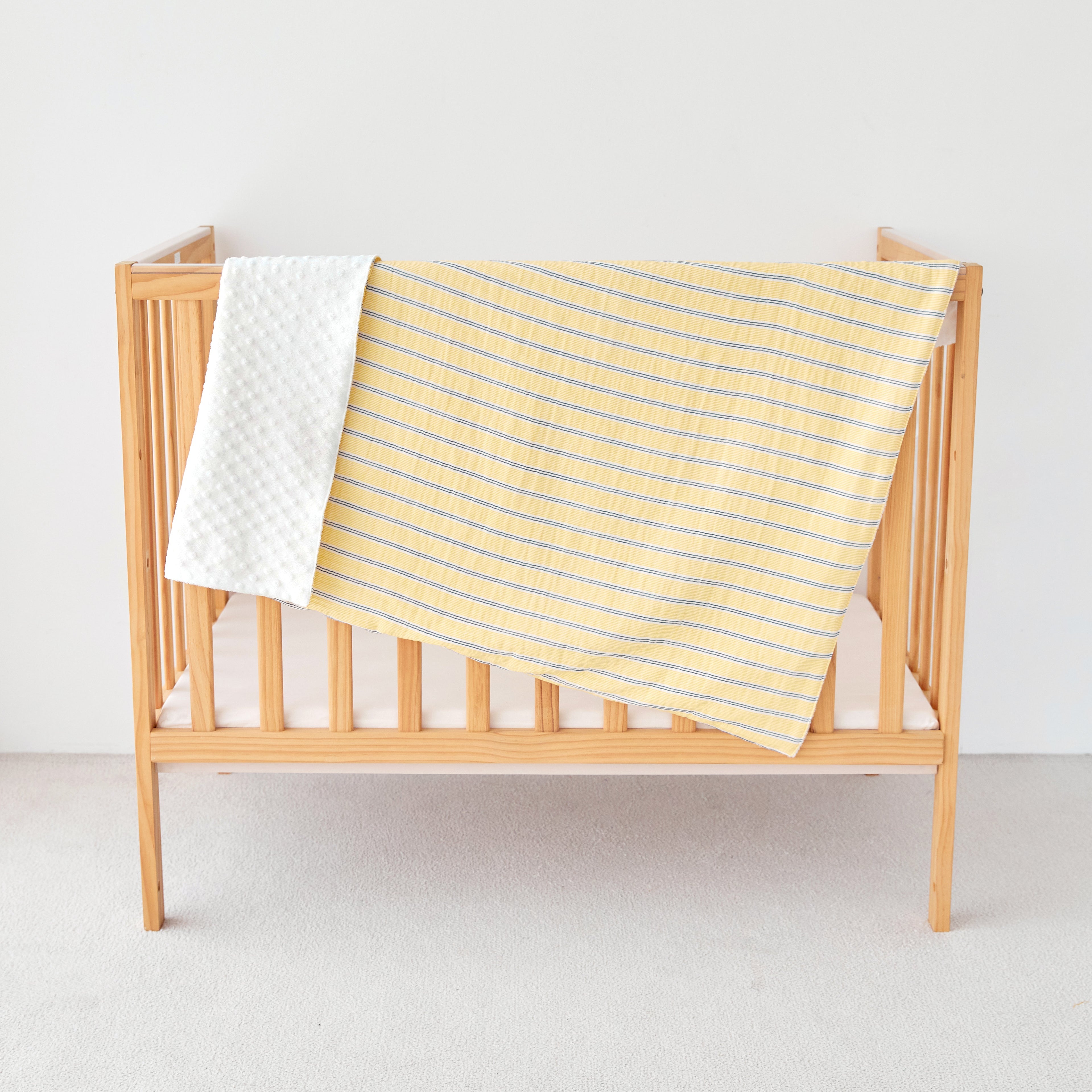 Wooden crib with a yellow baby striped  gauze minky blanket on a light background